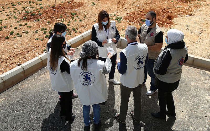 À l’extérieur, un groupe de huit personnes debout en cercle discutent. Elles portent un gilet beige portant le logo bleu de la Fondation Mérieux sur le dos.