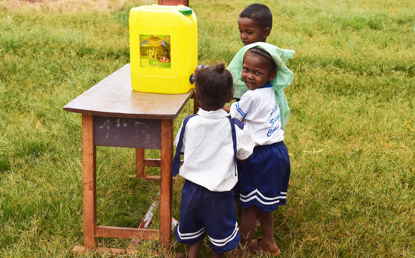 Trois petites filles malgaches se lavent les mains à partir d’un bidon d’eau.