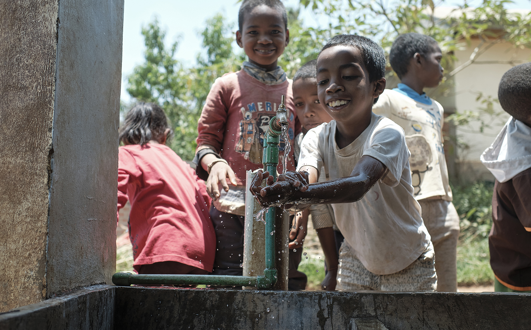 Des enfants malgaches se lavent les mains dans une cuve à l’extérieur, de face.
