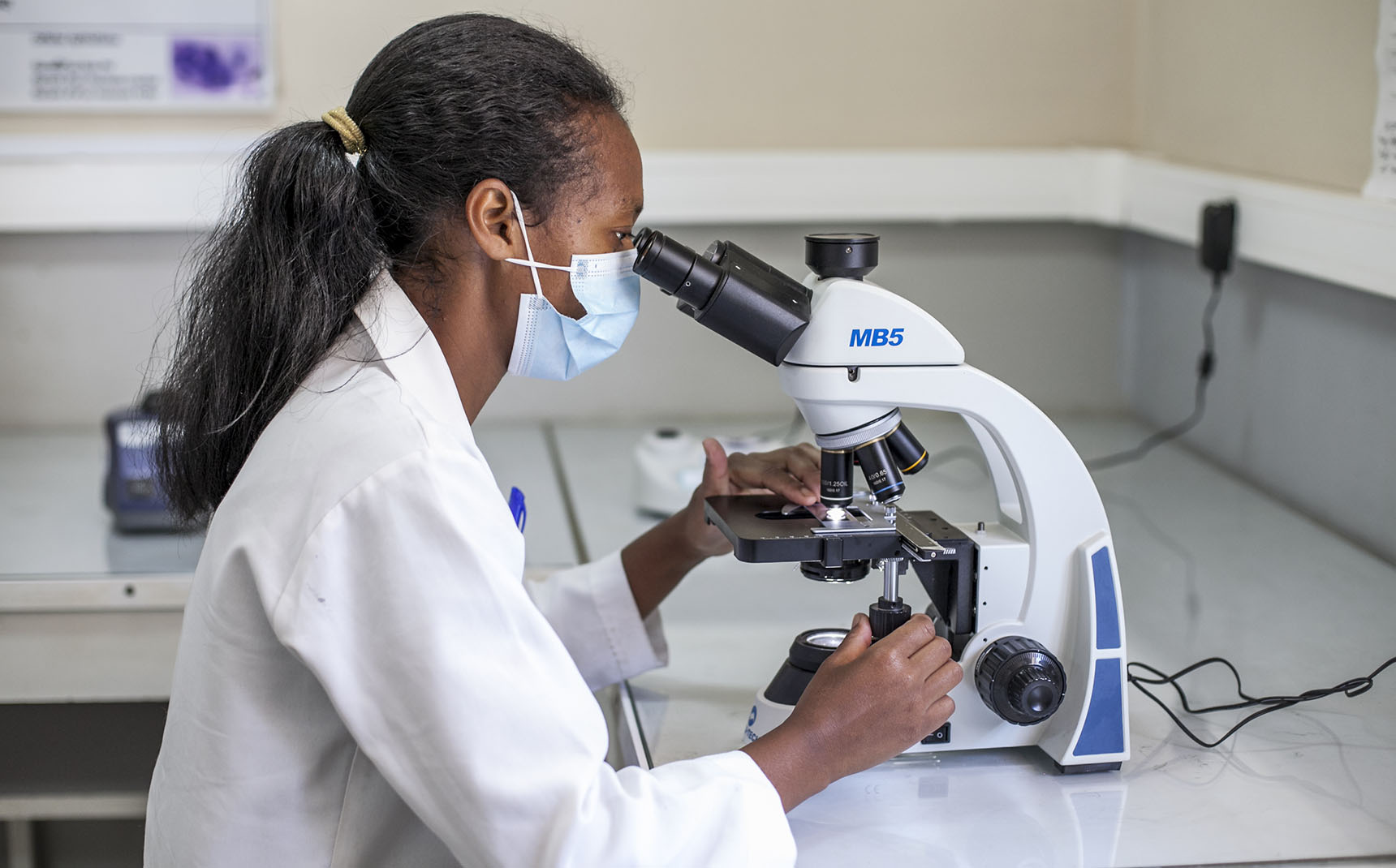 Une laborantine de profile utilise un microscope.