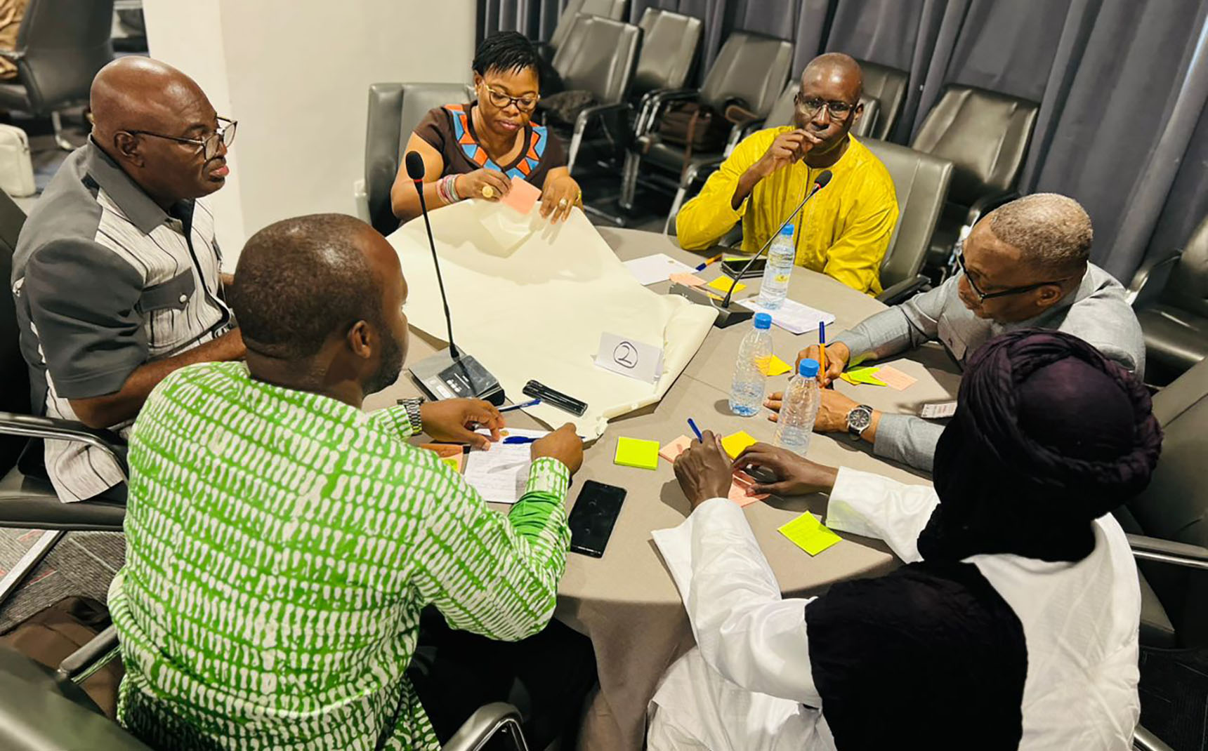 Six personnes sont assises autour d’une table ronde et écrivent sur une grande feuille.