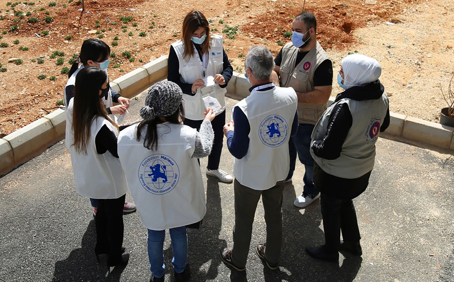 Un groupe de personnes forment un cercle, elles portent des gilets avec le logo de la Fondation Mérieux.