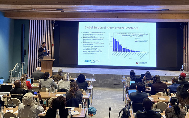 Participants sat in rows in a conference room listening to a presentation with a video projection on a screen