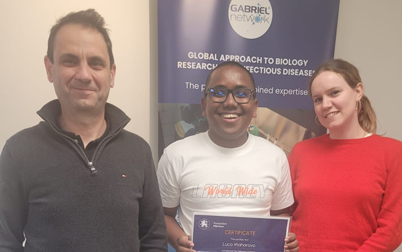 Trois personnes se tiennent devant un kakemono portant le logo du Reseau GABRIEL, la personne du milieu tient dans ses mains le certificat de la formation