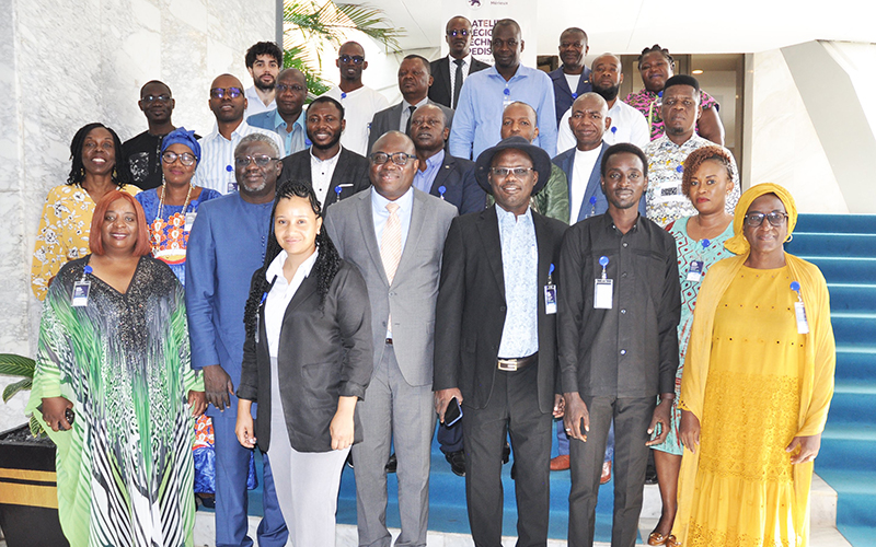 Groupe de personnes pose debout à l'extérieur sous un préau blanc.