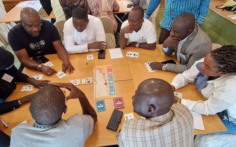 Groupe de personnes assis autour d’une table en bois, jouant à un jeu de cartes pédagogiques lors d’un atelier.